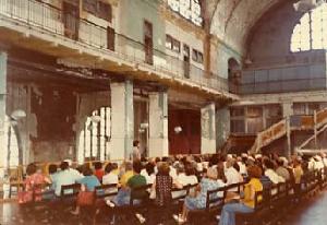 Bernardin addressing a tour in the unrestored Great Hall. Note damaged walls and old stairs and barriers in place from the post-immigration period.